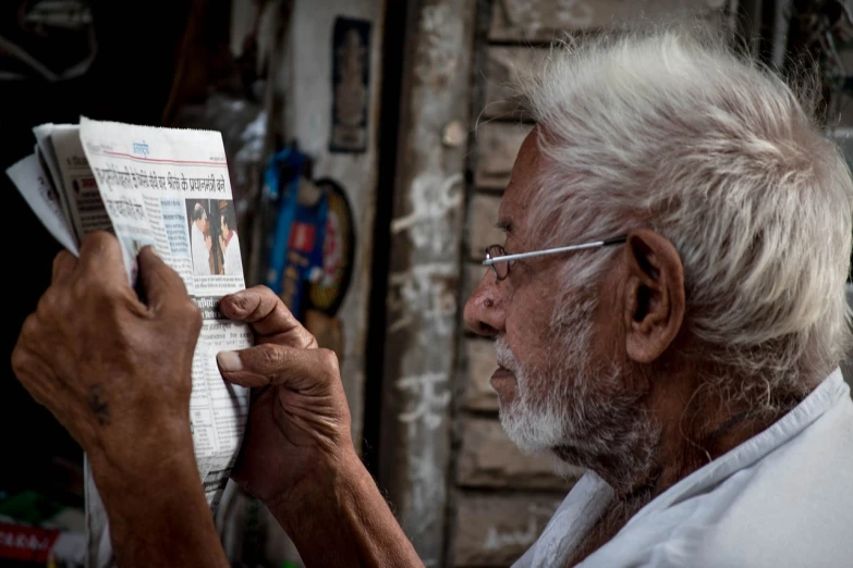 a man reading a newspaper while wearing glasses, a picture, pexels contest winner, wise old indian guru, in an alley, oldman with mustach, shot on sony a 7