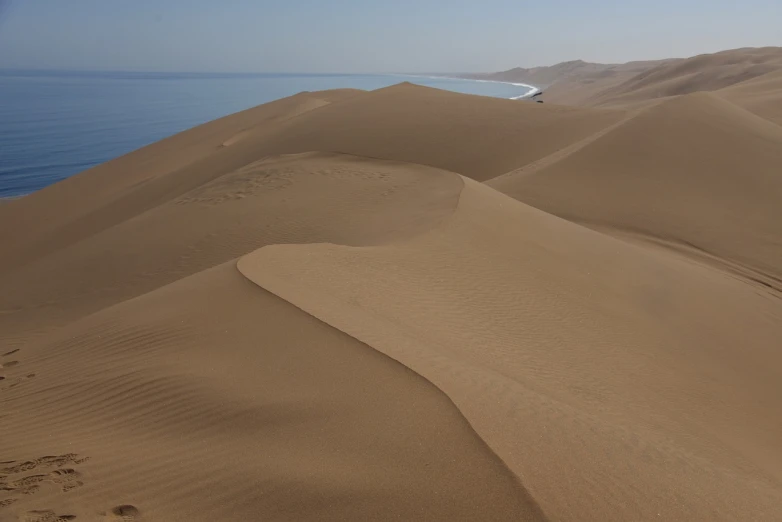 a view of some sand dunes with a body of water in the distance, by Etienne Delessert, flickr, peruvian, south african coast, sinuous, taras susak