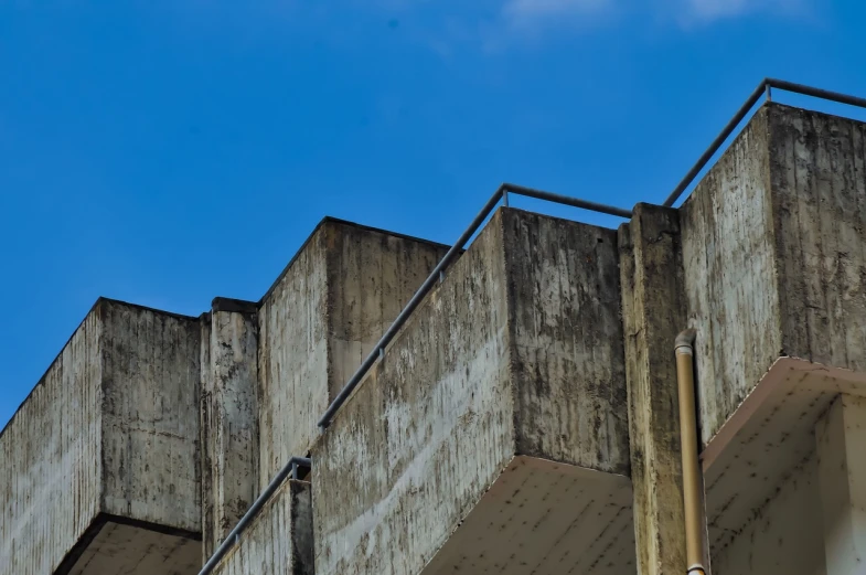 a clock that is on the side of a building, brutalism, lost place photo, cinematic view from lower angle, deep blue sky, concrete balcony