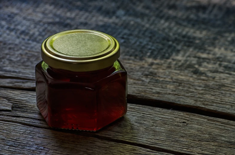 a jar of honey sitting on a wooden table, a picture, by Franz Hegi, pixabay, jelly - like texture, stock photo, hexagonal shaped, cherry