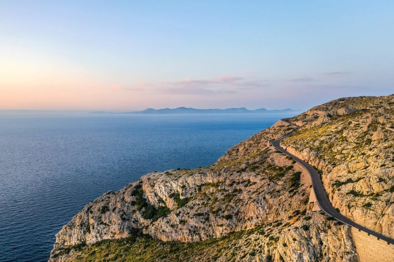 a train traveling along the side of a mountain next to the ocean, by Julian Allen, shutterstock, croatian coastline, sunset panorama, natural stone road, very wide wide shot