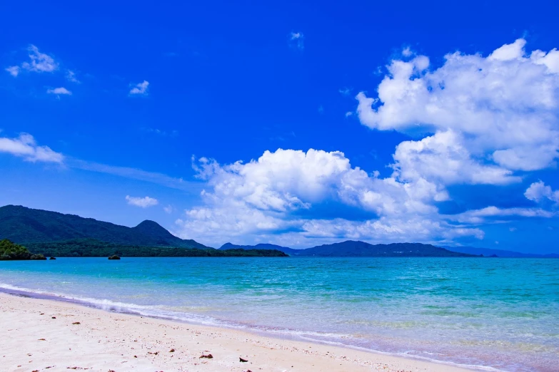 a large body of water sitting on top of a sandy beach, a photo, by Tadashi Nakayama, shutterstock, okinawa japan, blue colours, wide establishing shot, under blue clouds