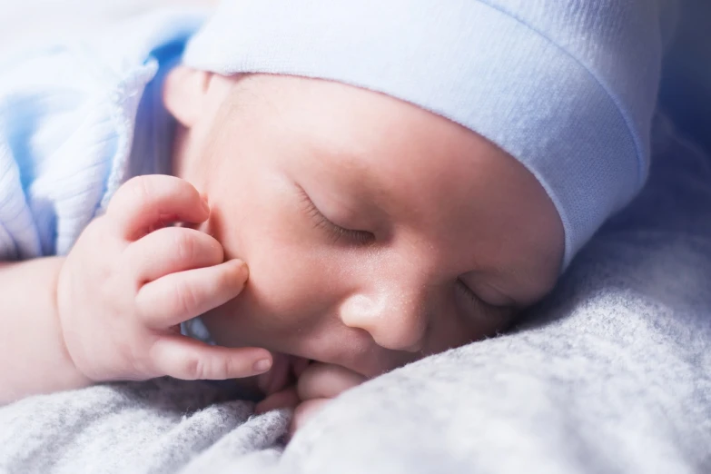 a close up of a baby sleeping on a blanket, by Juan O'Gorman, pexels, digital art, hand on his cheek, relaxed. blue background, small straight nose, istockphoto