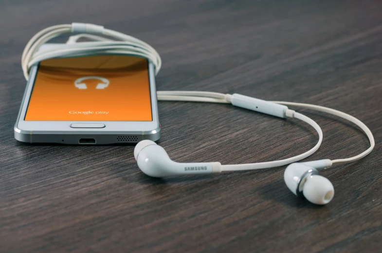 a cell phone sitting on top of a wooden table, an album cover, pexels, orange metal ears, orange and white color scheme, earbuds, cable plugged in
