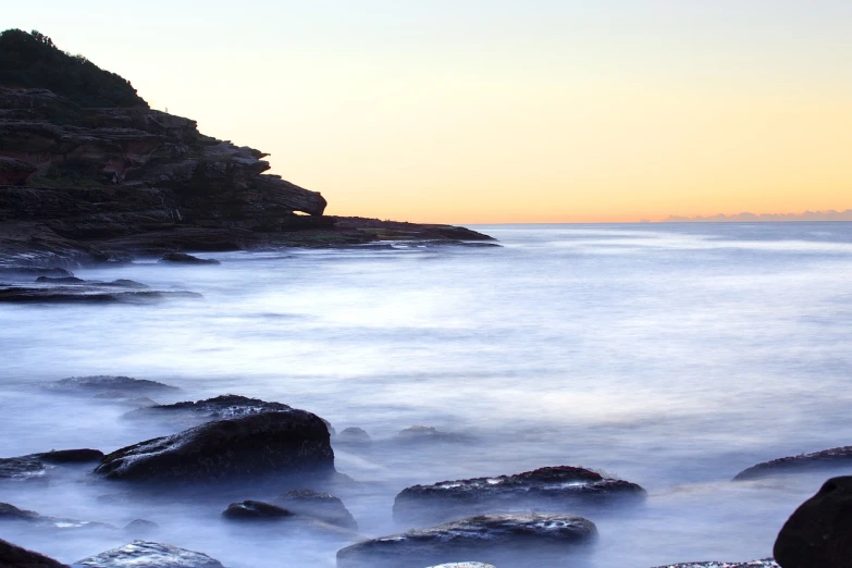 a body of water with rocks in the foreground, by Robert Sivell, minimalism, manly, istock, in the early morning, silky