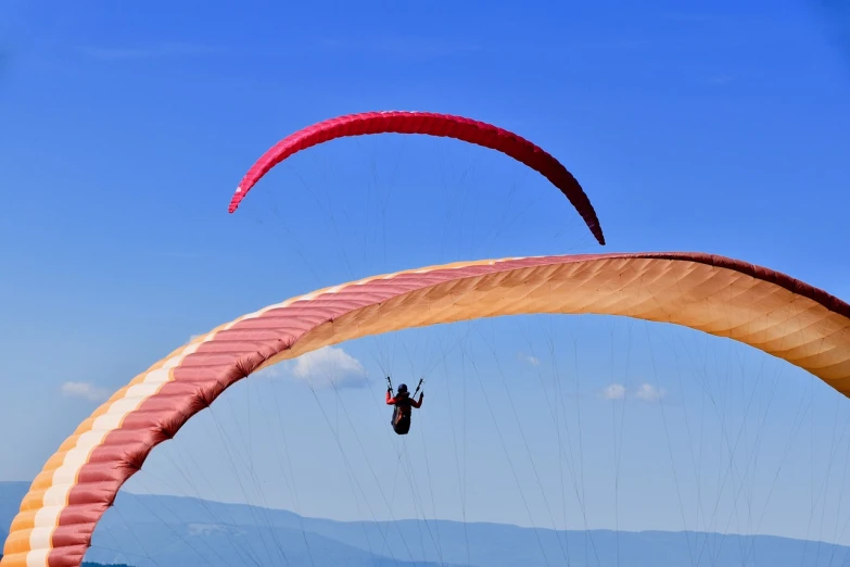 a couple of people that are parasailing in the sky, a picture, shutterstock, insect wings, blue and red color scheme, over the hills, set photo