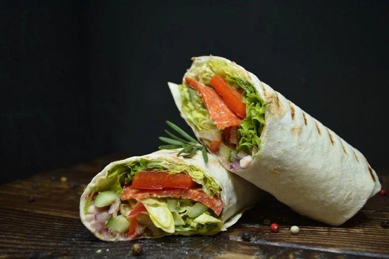 a cut in half sandwich sitting on top of a wooden table, a picture, by Koloman Sokol, shutterstock, cloth wraps, on black background, kebab, salmon