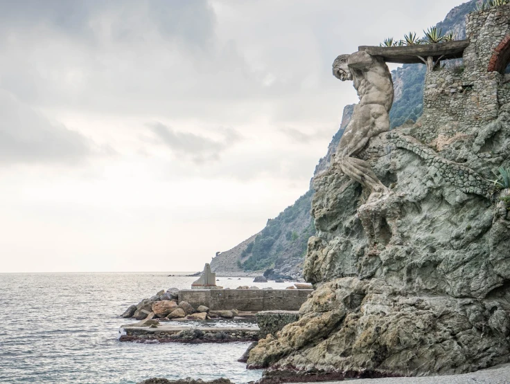 a statue sitting on top of a cliff next to the ocean, a statue, by Giorgio Cavallon, nice slight overcast weather, cinq terre, prometheus, right side composition