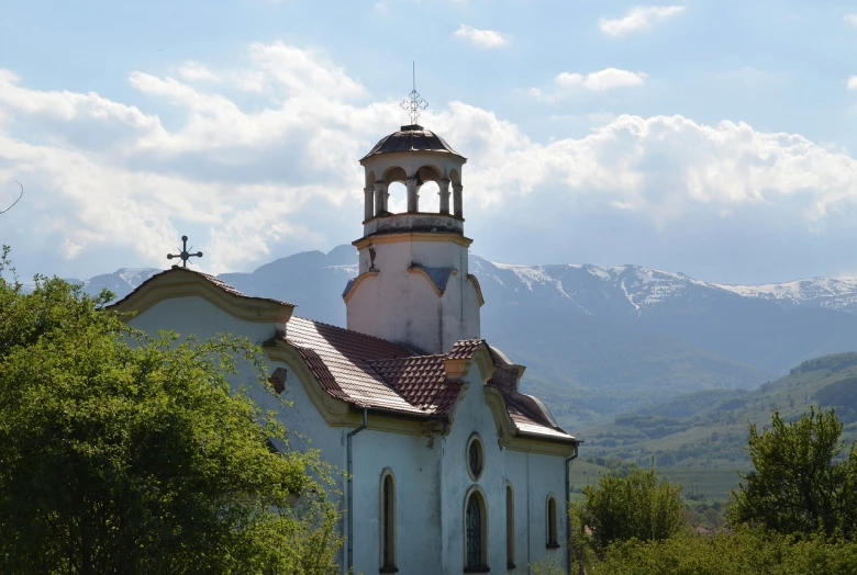 a church with a steeple in front of a mountain range, a picture, by January Suchodolski, shutterstock, in orthodox church, view from side, can basdogan, many details