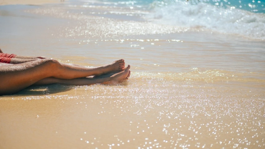 a woman sitting on top of a sandy beach next to the ocean, pexels, shiny wet skin!!, legs, sparkling in the sunlight, 1 4 9 3