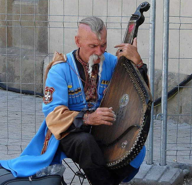 a man sitting on the ground playing a musical instrument, a photo, by Eugeniusz Zak, trending on pixabay, wearing authentic attire, harness, cyan, huge blond moustache