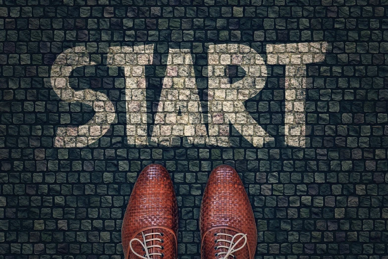 a pair of brown shoes standing in front of a sign that says start, by Kurt Roesch, happening, brick, background image, photostock, mosaic floor