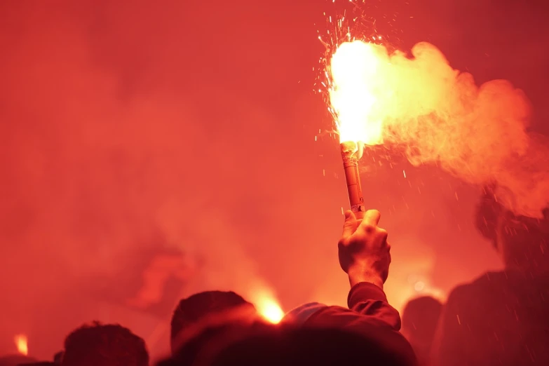 a person holding a sparkler up in the air, a picture, by Kazimierz Wojniakowski, shutterstock, renaissance, football hooligans, holding a red banner, workers revolution, with red haze