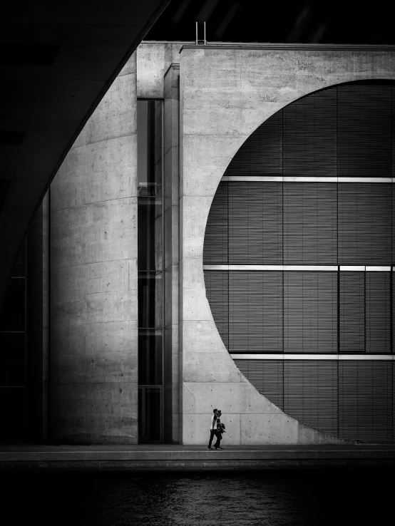 a person sitting on a bench in front of a building, by Joze Ciuha, minimalism, circle forms, oscar niemeyer, fan ho photography, man walking
