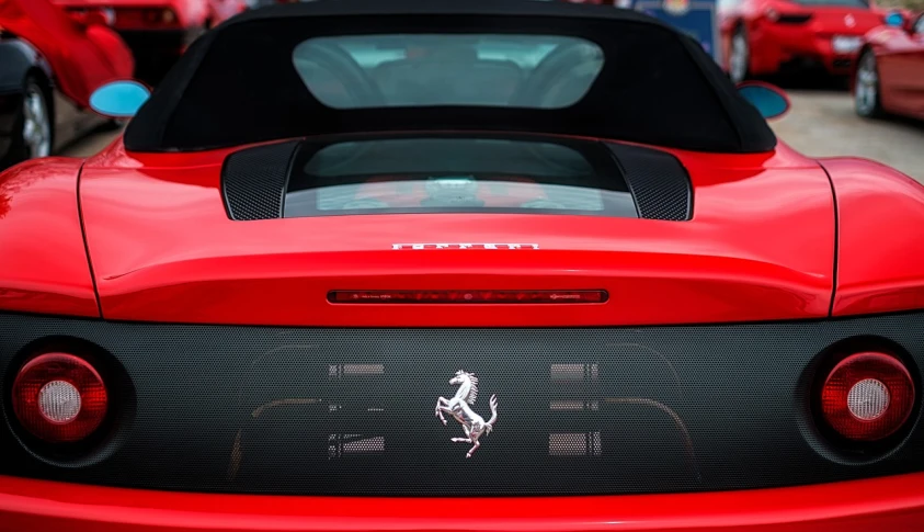a red sports car parked in a parking lot, a picture, inspired by Bernardo Cavallino, unsplash, renaissance, chest plate with ferrari logo, back lit, riding on a prancing horse, close-up shot from behind