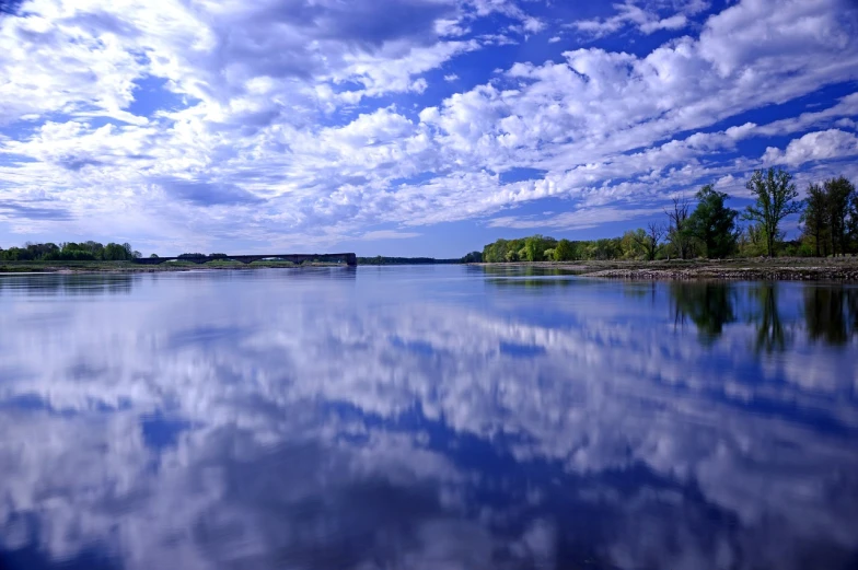 a large body of water with a bridge in the background, by Jan Rustem, flickr, beautiful sky with cumulus couds, iowa, sharp detailed reflections, springtime morning