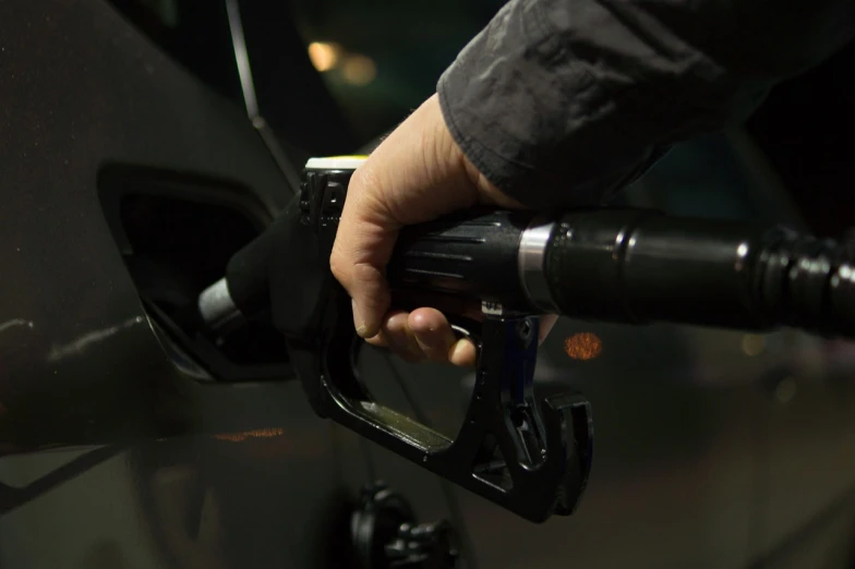 a person pumping gas into a car at a gas station, a picture, pexels, photorealism, on a dark background, holding shotgun down, inspiration, shiny silver