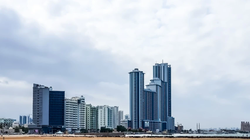 a man flying a kite on top of a sandy beach, a tilt shift photo, colombo sri lanka cityscape, vertical architecture, viewed from the harbor, tall minimalist skyscrapers