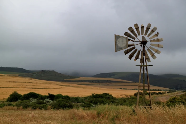 a windmill in a field on a cloudy day, a picture, by Arie Smit, pexels, land art, cape, screen capture, photograph credit: ap, grain”