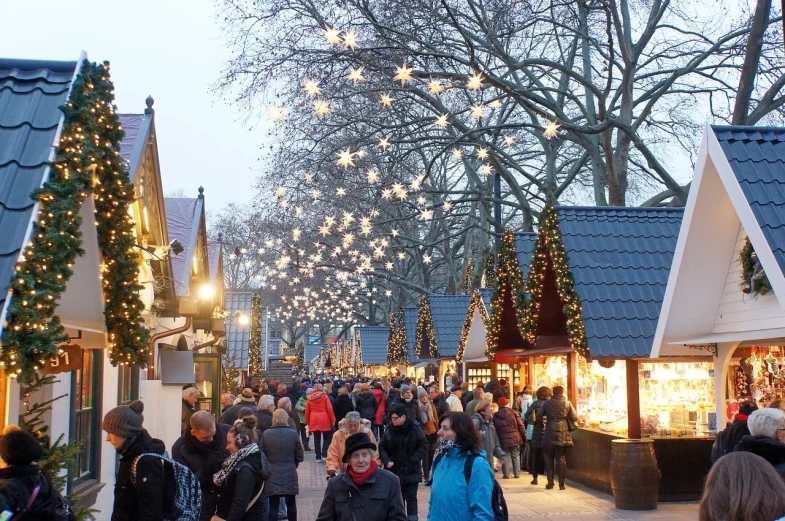 a large group of people walking down a street, a photo, by Jakob Gauermann, shutterstock, winter wonderland, some stalls, full trees, daniel libeskind