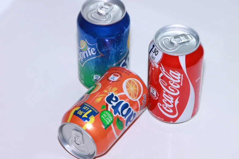 three soda cans sitting next to each other on a table, a picture, flickr, some orange and blue, brazil, no gradients, drinking a bottle of coca-cola