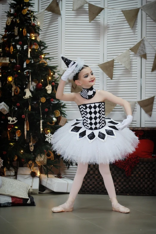 a young ballerina standing in front of a christmas tree, a portrait, inspired by Elizabeth Polunin, shutterstock, arabesque, checkered motiffs, high quality costume, harley queen, white and black