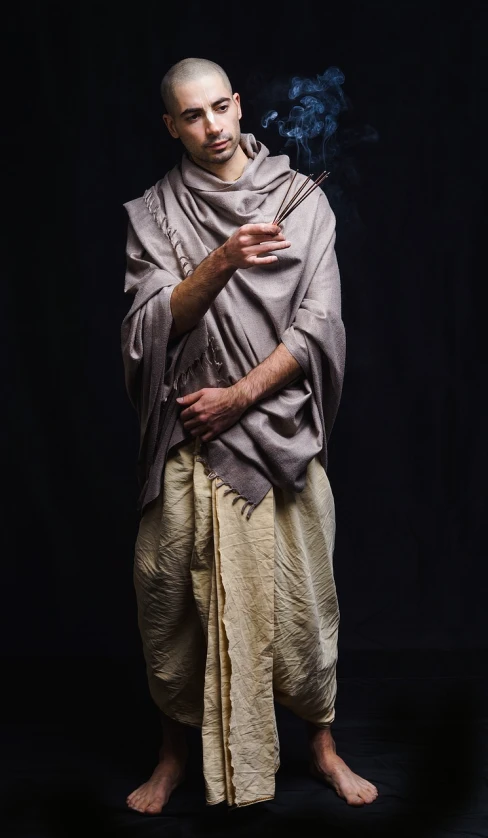 a man with a cigarette in his hand, inspired by Jan Lievens, renaissance, draped in flowing fabric, real life photo of a syrian man, thin male alchemist, pharaoh clothes