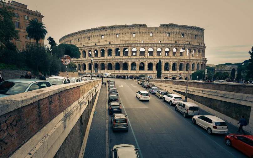 a street filled with lots of traffic next to a tall building, a tilt shift photo, by Alessandro Allori, renaissance, in a coliseum, car, coliseum of rome, retro effect