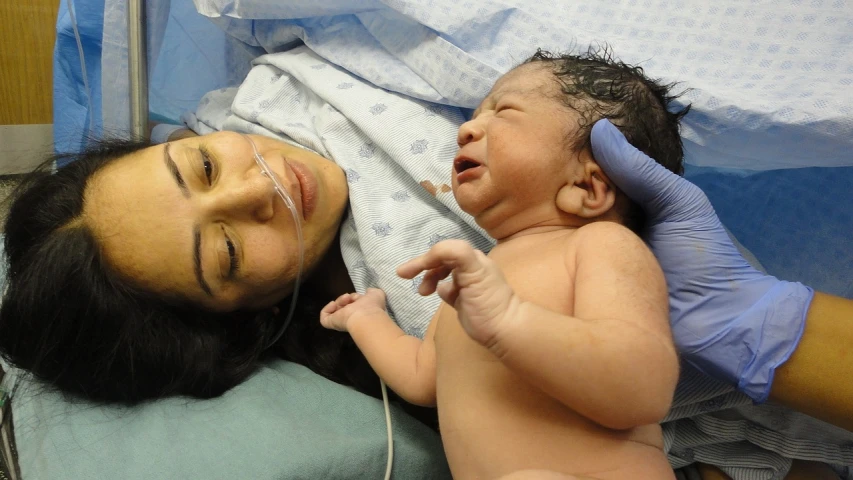 a woman laying next to a baby in a hospital bed, a photo, happening, hand transplanted to head, hopeful expression, seen from above, an olive skinned