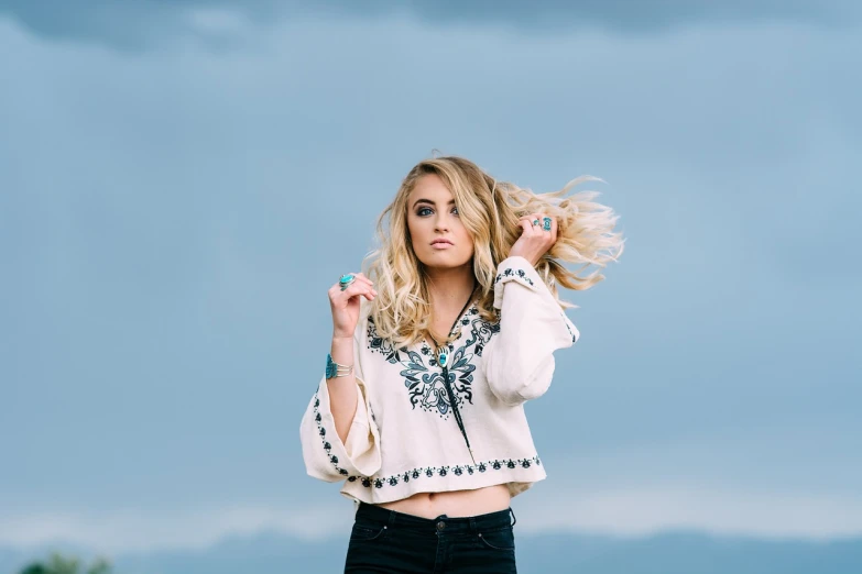 a woman standing on top of a lush green field, a portrait, by Sydney Carline, trending on pexels, arabesque, blonde hair blue eyes, windy floating hair!!, at a fashion shoot, behind that turquoise mountains