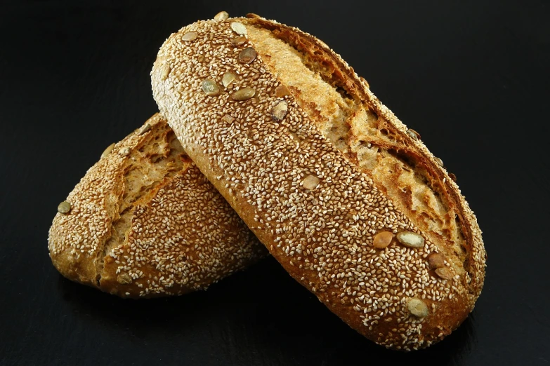 two loaves sitting next to each other on a table, inspired by Normand Baker, pixabay, luscious with sesame seeds, on black background, photo-realistic maximum detail, german