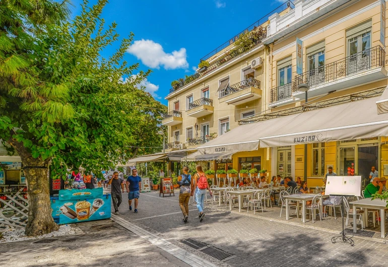 a group of people walking down a street next to tall buildings, a photo, by Mathias Kollros, shutterstock, fine art, at ancinet agora of athens, in a bright cafe, rich picturesque colors, summer street near a beach