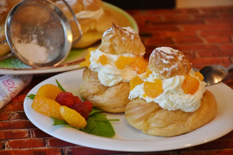 a couple of pastries sitting on top of a white plate, by David Garner, shutterstock, baroque, whipped cream on top, orange and white, hawaii, crispy buns