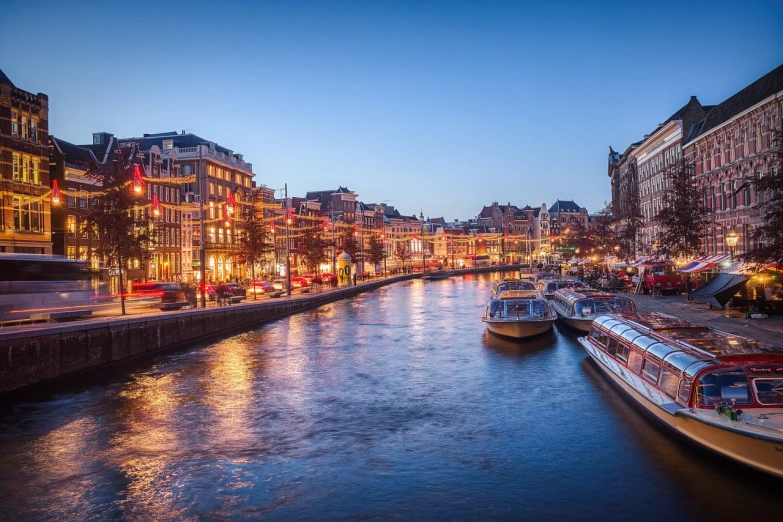 a river filled with lots of boats next to tall buildings, by Jakob Gauermann, shutterstock, art nouveau, blue hour lighting, amsterdam, stock photo, parisian street at night