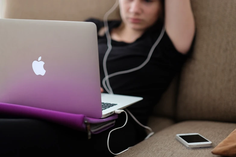 a woman sitting on a couch with a laptop and headphones, by Joe Bowler, pexels, apple logo, purple and black, wikimedia commons, teenager girl