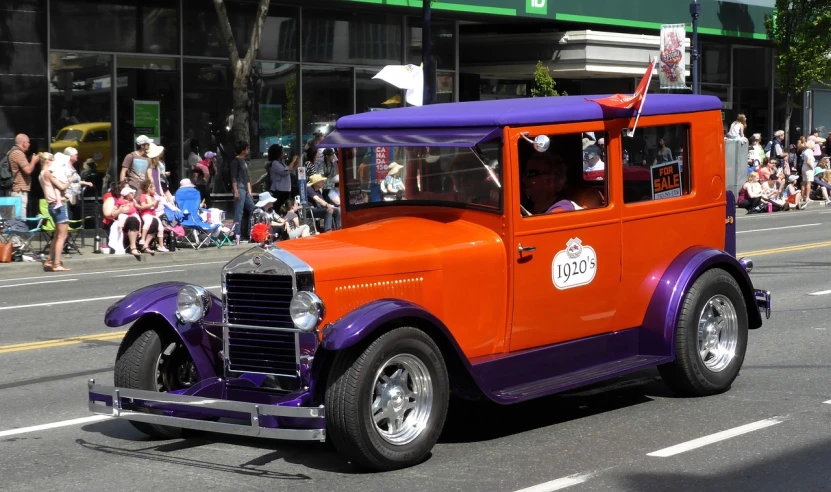 an orange and purple truck driving down a street, by Jim Nelson, flickr, jazz age, the ugliest car in the world, kidmo!!!, parade setting