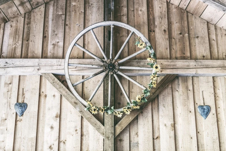 a wagon wheel hanging from the ceiling of a barn, by Emma Andijewska, with yellow flowers around it, high resolution details, ceremony, wild west background