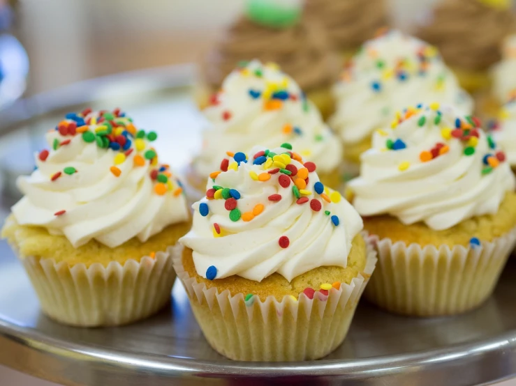 a plate of cupcakes with white frosting and sprinkles, a picture, by Dietmar Damerau, pexels, istockphoto, close up angle, benjamin vnuk, snacks