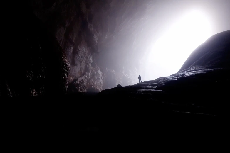 a person standing at the end of a cave, lightshafts and foggy atmosphere, epic scale ultrawide angle, video still, humans exploring