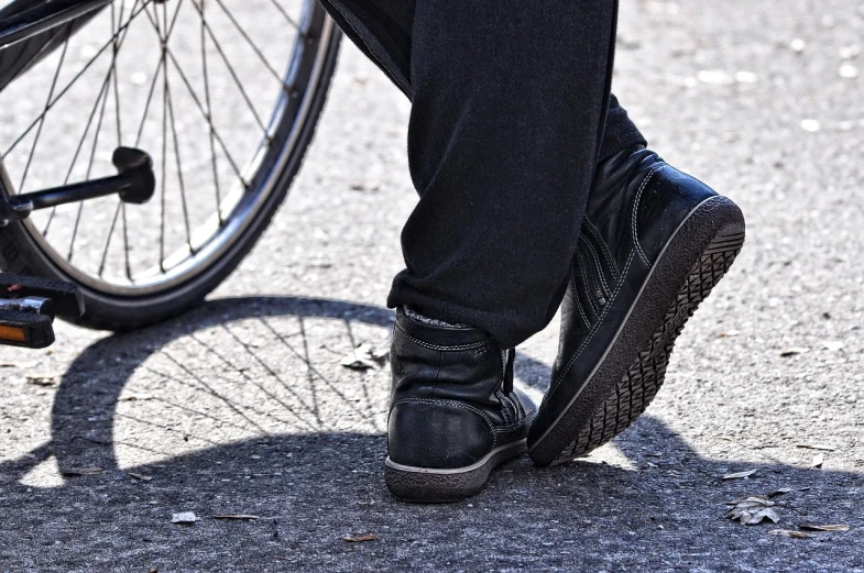 a person standing next to a bike on a street, pixabay, gum rubber outsole, baggy black pants, dynamic closeup, politics