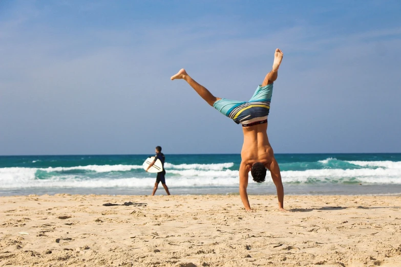 a man doing a handstand on the beach, by Niko Henrichon, arabesque, surfing, istock, on the beach at noonday, on a hot australian day