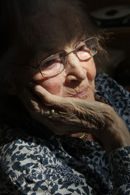 a close up of a person wearing glasses, by Kazimierz Wojniakowski, nursing home, hand on her chin, with backlight, taken in the late 2010s