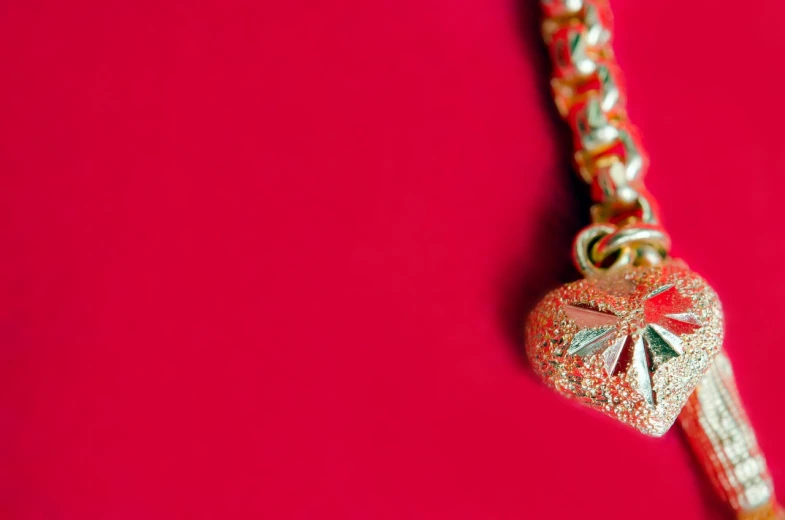 a close up of a chain with a heart on it, inspired by János Valentiny, hurufiyya, red background, golden ribbon, closeup - view, colorful adornments