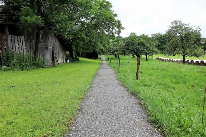 a path in the middle of a field with a barn in the background, by Kiyoshi Yamashita, wide greenways, sidewalk, rainny, 2 0 2 2 photo