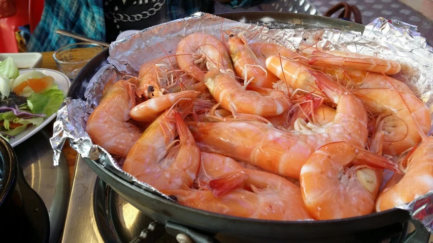 a pan filled with shrimp sitting on top of a table, by Victoria Francés, hurufiyya, at a beach party in ibiza, shiny skin”, braziers, viewed from below