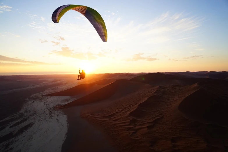 a person that is flying a kite in the sky, a picture, by Peter Churcher, shutterstock, desert sunrise in the background, on dune, gliding, highly detailed 8k photography