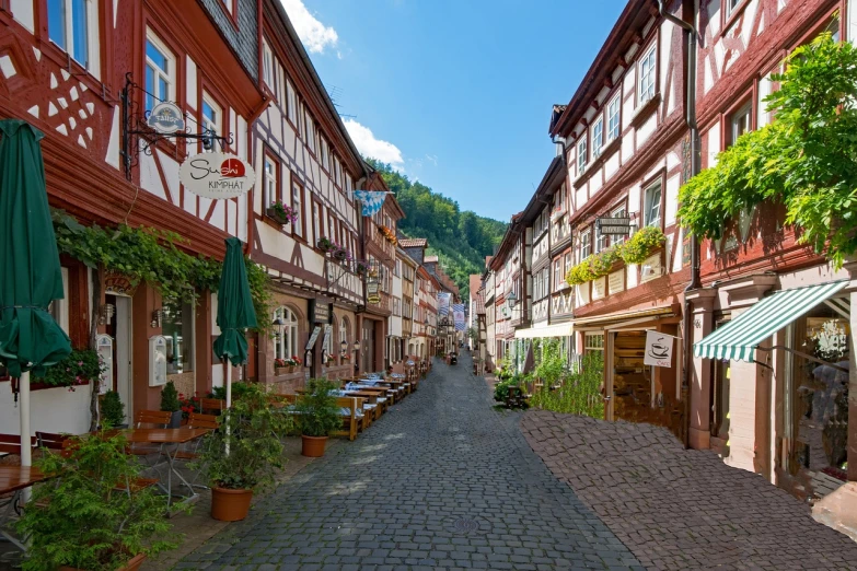 a narrow cobblestone street with tables and umbrellas, a photo, by Juergen von Huendeberg, shutterstock, black forest, hills, wooden, stock photo