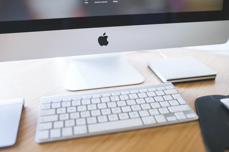 a computer monitor sitting on top of a wooden desk, by Adam Rex, pexels, apple logo, white and silver, mechanical keyboard, highly detailed rounded forms