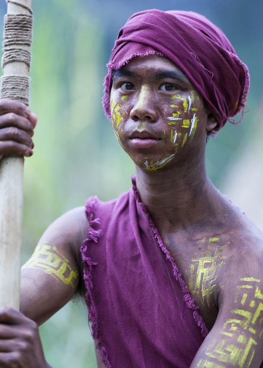 a man with yellow paint on his face holding a stick, a portrait, by Robert Brackman, shutterstock, myanmar, maroon, covered in runes, 4k photo”