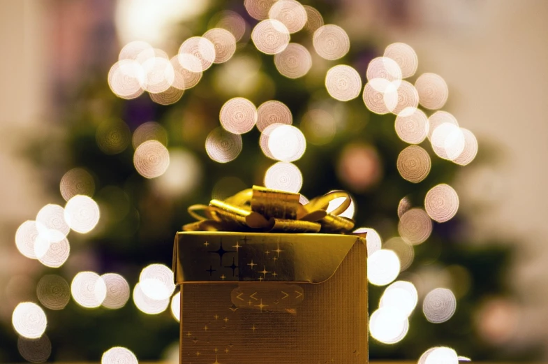 a gold gift box sitting in front of a christmas tree, a picture, by Maksimilijan Vanka, pixabay, 4 5 mm bokeh, istockphoto, lighting, discovered photo